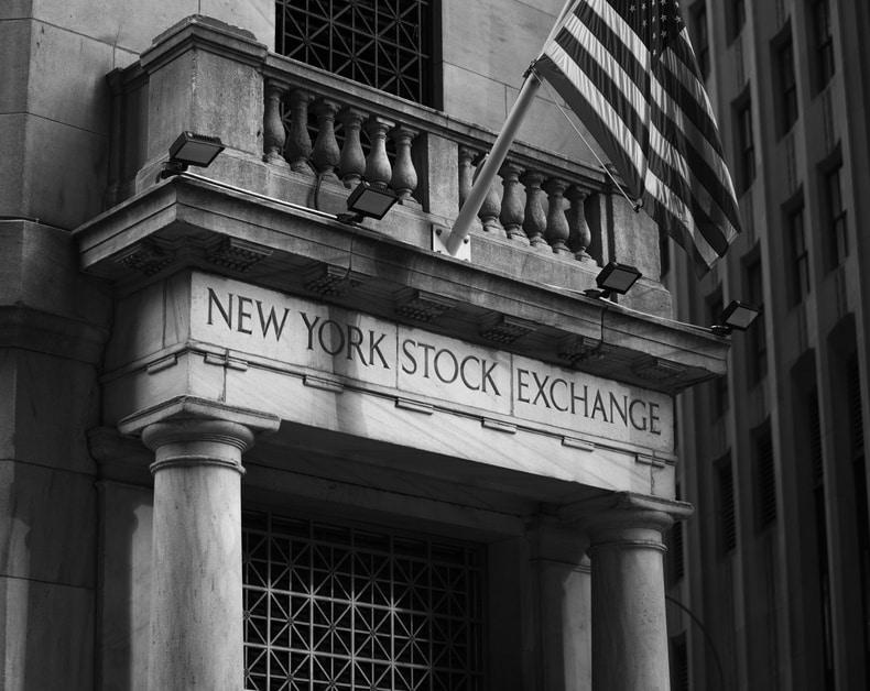 Black-and-white photo of the New York Stock Exchange entrance with tall columns and an American flag above the doorway.