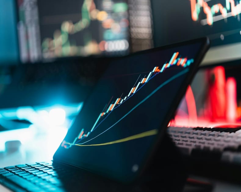 Laptop displaying a Candlestick stock chart with rising and falling lines on a dark screen.