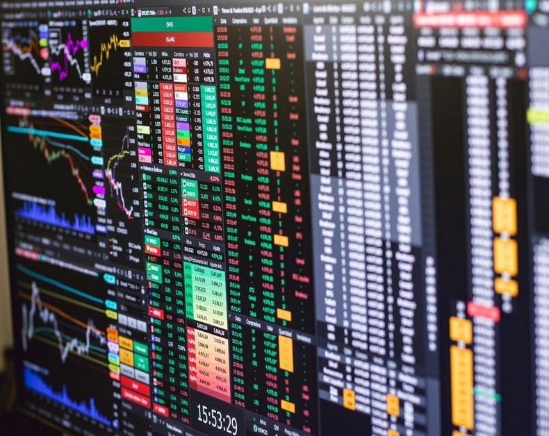 Multiple monitor dashboards displaying stock charts, price tables, and market data in green and red colors.