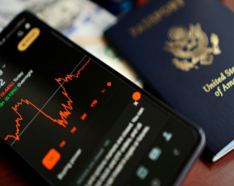 Phone displaying a red stock chart beside a United States passport in the background.