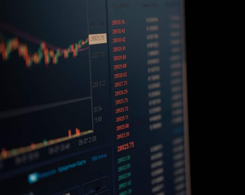 Close-up of a dark monitor displaying a stock chart with candlesticks and red price numbers.