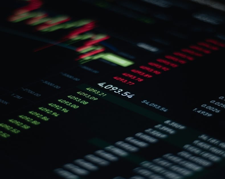 Dark stock market screen with glowing green and red numbers and charts, showing financial data and prices.