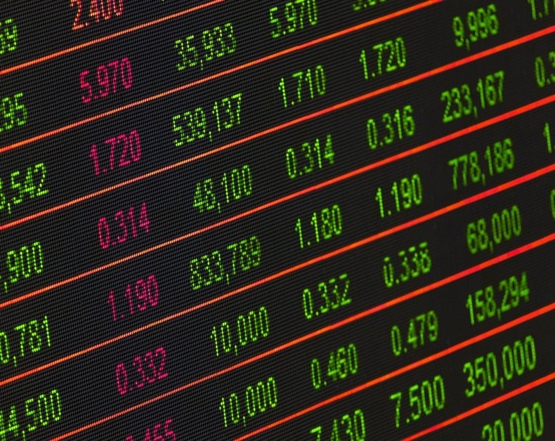 Close-up of a stock ticker display with green and red numbers representing prices and changes on a dark grid background.