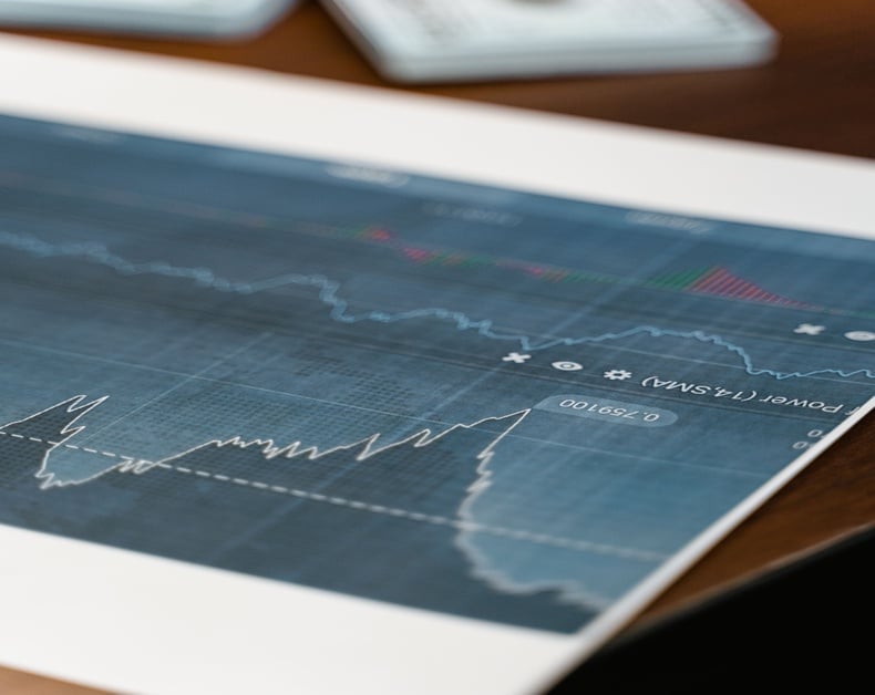 Blue financial chart with fluctuating stock lines on a desk, calculator blurred in the background.