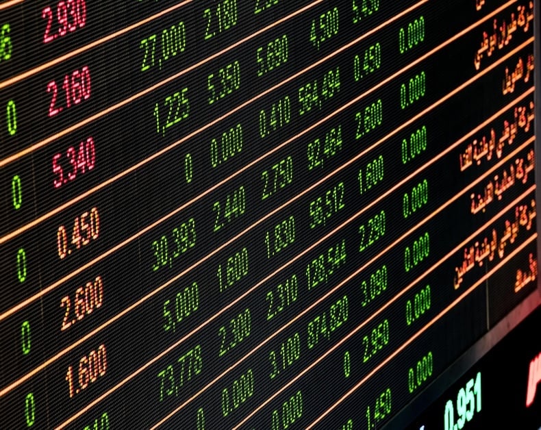 Electronic stock board displaying fluctuating prices in green and red, with numeric values and percentages cascading across rows.