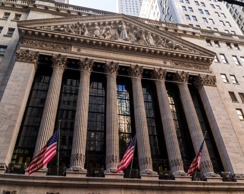 Front view of the New York Stock Exchange building with six tall Corinthian columns, flags, and a sculpted pediment on top.