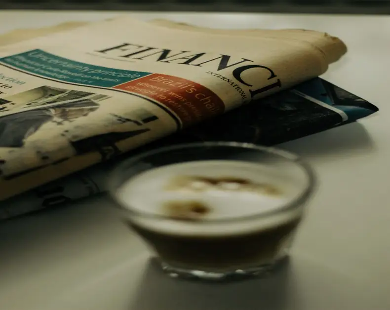 A folded newspaper resting on a table with a small espresso cup in the foreground.